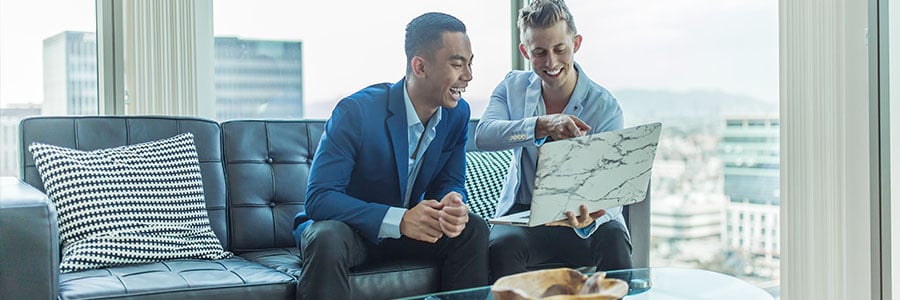 Two business persons sitting on a couch view a laptop.