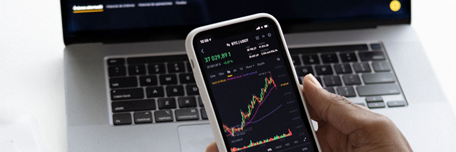 A hand holding a mobile device with a graph chart is held above a laptop.